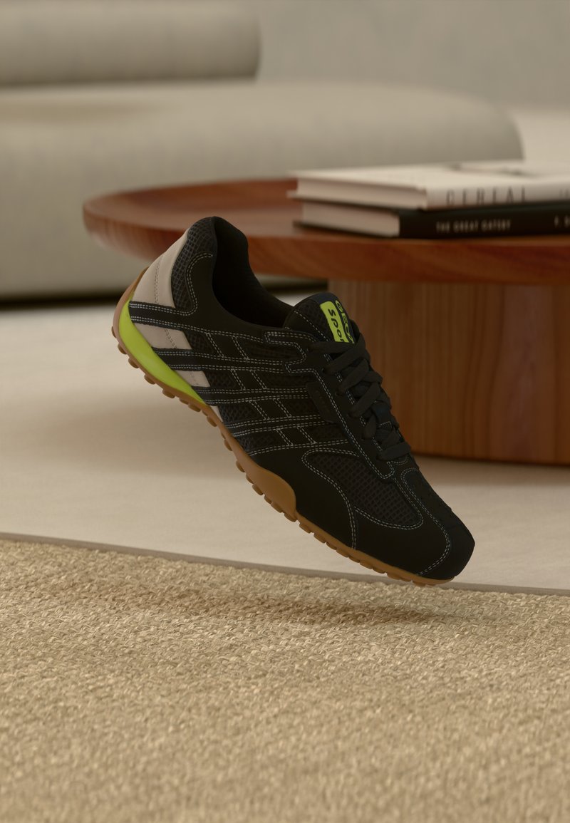 Chaussure de sport noire avec des accents verts, en mesh et matériau synthétique, semelle en caoutchouc texturée, présentant des surpiqûres contrastantes et un design élégant.