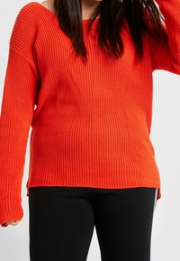 Maglione a coste rosso con maniche lunghe e design scollato, caratterizzato da una vestibilità comoda e spacchi laterali all'orlo.