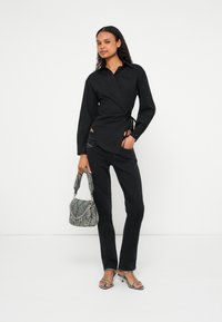 Μαύρο πουκάμισο τύπου wrap με μακριά μανίκια, συνδυασμένο με εφαρμοστές μαύρες τζιν. Κρατά μια γκρι υφασμάτινη τσάντα και φορά σανδάλια με λουράκια.