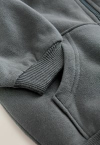 Mörkgrå sweatshirtmaterial med ribbad mudd och ficka, med en mjuk textur och subtila sömdetaljer.