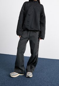 Svart vadderad pullover med texturerad design, hög krage och framdragkedja. Matchande svarta byxor med sidostripes och gråa träningsskor.