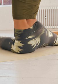 Visoke tajice u tamnozelenoj i crnoj boji s motivom tie-dye. Izrađene su od rastezljivog materijala, a na pojasu se nalazi logotip.