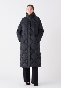 Schwarzer, langer Daunenmantel mit einem rautenförmigen Steppmuster, hohem Kragen und seitlichen Taschen. Glattes Material mit matter Oberfläche.