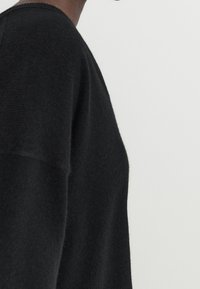 Black wool sweater with a soft texture, featuring a round neckline and dropped shoulders, displayed from a side angle.