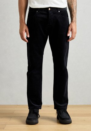 Black corduroy pants featuring a straight-leg design, pocket detailing, and paired with black shoes on a wooden floor.