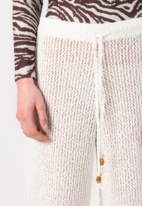 Pantalones de punto blancos con un tejido suelto y abierto, que cuentan con una cinturilla texturizada y un cordón con acentos de cuentas de madera.
