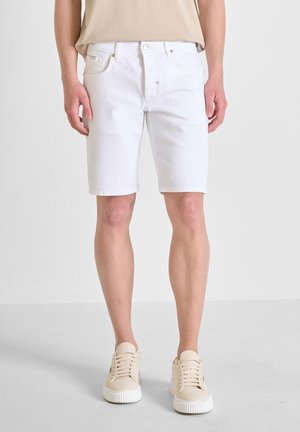 Shorts en denim blanc avec une coupe classique à cinq poches, dotés d'un zip et de coutures discrètes, associés à des baskets beiges.