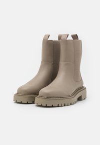 Botas de tobillo beige con parte superior de cuero liso y paneles elásticos laterales. Suela de goma gruesa y resistente con un acabado texturizado. Doble tirador.