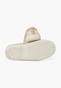 Zapatos slip-on de malla dorada con una suela de goma blanca texturizada. La parte superior presenta un diseño transpirable con sutiles acentos de costura.