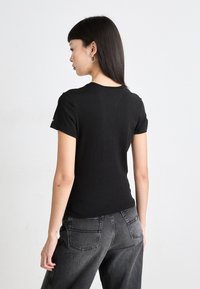 Svart t-skjorte med kort erme og rund hals, laget av myk stoff, vist fra baksiden. Kombinert med høyt midje mørkegrå jeans.