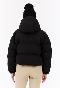 Čierna nafúknutá bunda s vysokým golierom a skráteným strihom. Má zúžené manžety a hladký povrch. Kombinovaná s béžovými nohavicami.