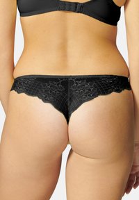 Femme vue de dos, mettant en avant le bas du dos et les hanches, portant un string en dentelle noire et un soutien-gorge assorti.