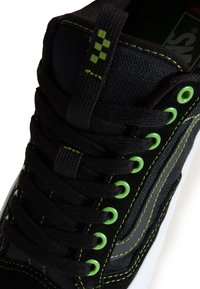 Baskets noires avec une tige en toile et des accents verts, couture contrastante, lacets ronds et œillets verts. Semelle en caoutchouc plate.