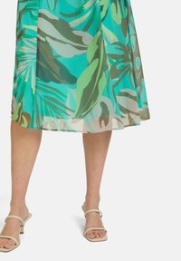 Kwiecista sukienka midi w turkusowych i zielonych odcieniach, z dużymi wzorami liści. Połączona z neutralnymi, wiązanymi obcasami. Lekki, zwiewny materiał.