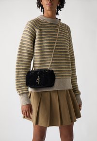 Borsa a tracolla nera trapuntata con catena dorata, indossata con un maglione lavorato a maglia a righe beige e verdi, abbinato a una gonna plissettata color khaki.