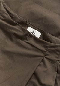 pruun kangas, millel on sile tekstuur, eristub õmmeldud saem ja sildiga, millel on must logo.