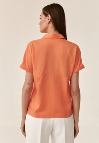 Blusa a maniche corte con colletto di un vivace arancione, dal texture morbido e con risvolti alle maniche, caratterizzata da un dettaglio con cucitura sul retro.