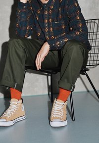 Sininen ruutupaita, jossa keltaisia timanttikuviota, tummanvihreät housut, oranssit sukat ja beiget korkeavartiset tennarit valkoisilla nauhoilla.