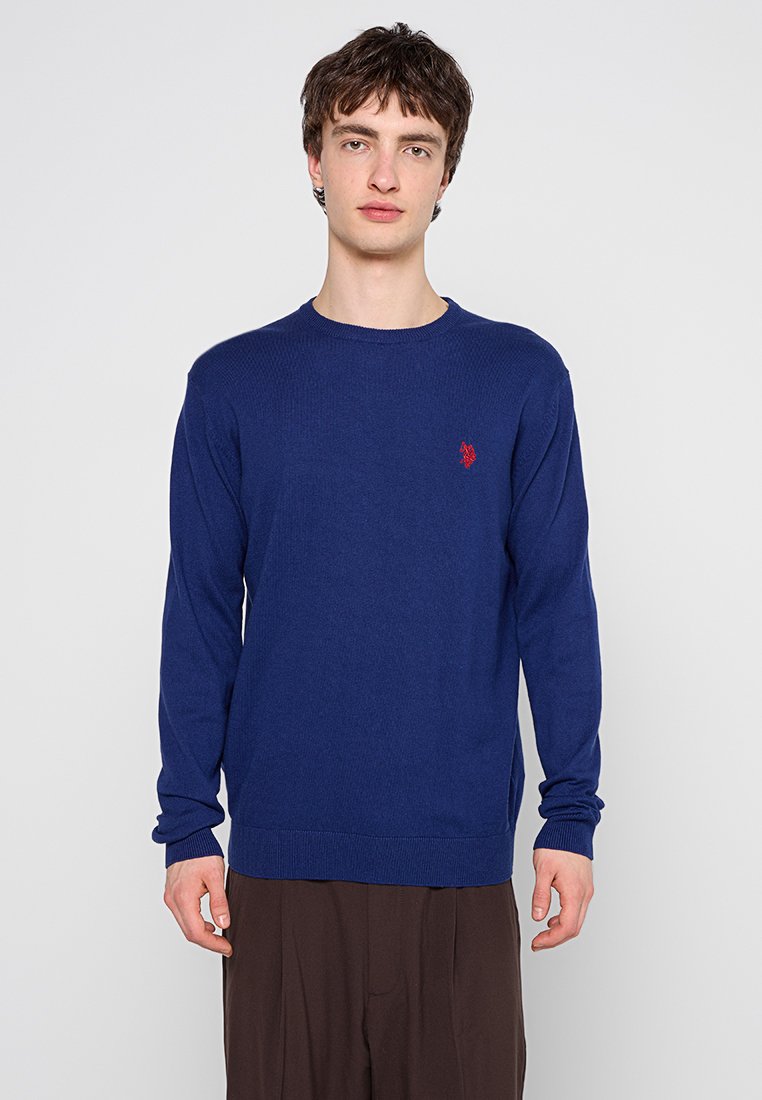 Navyblauer Strickpullover mit langen Ärmeln, rundem Ausschnitt und kleinem rotem Logo auf der Brust. Mit gerippten Bündchen und Saum.