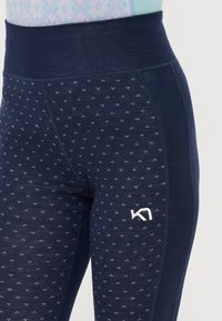 Mørkeblå leggings med høy linning, med et strukturert mønster av små prikker og en hvit logo på den nedre siden.