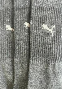 Drei Paar graue, gerippte Puma-Socken mit weißem Puma-Logo, nebeneinander ausgerichtet.