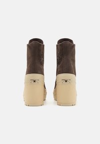 Brown leather ankle boots with a beige platform sole. Features a circular logo on the outer heel and branded tags on the back.