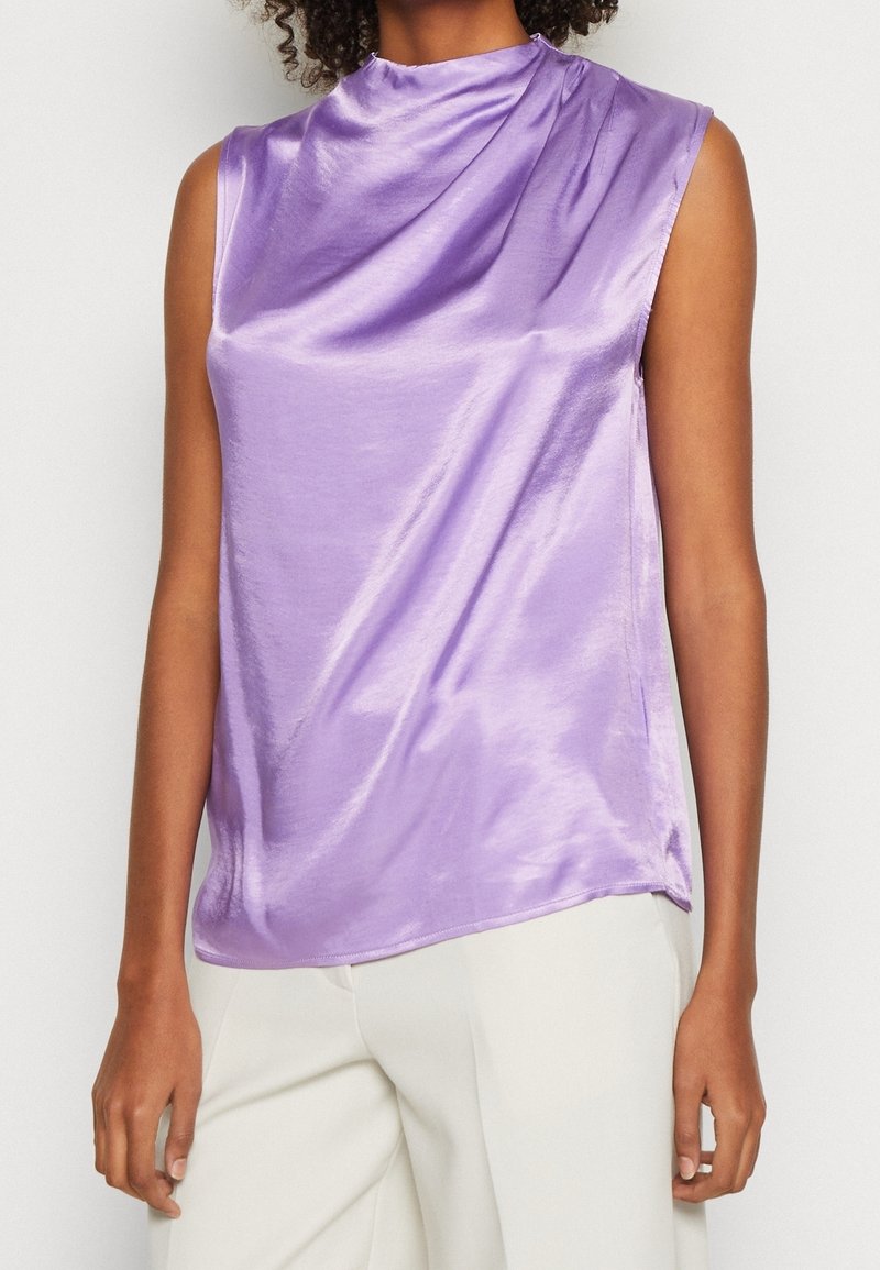 Haut sans manches violet en tissu satiné brillant, avec un col montant et un devant drapé, coupe ample et ourlet arrondi.