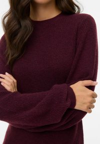 Texturovaný, tmavě vínový pletený svetr s dlouhými, mírně oversized rukávy a kulatým výstřihem, který má žebrovaný lem a manžety.