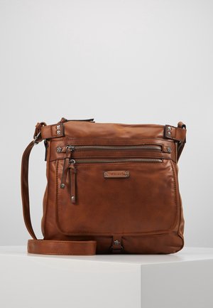 Sac bandoulière en cuir marron avec deux poches avant zippées et une sangle réglable, présenté sur un socle blanc.