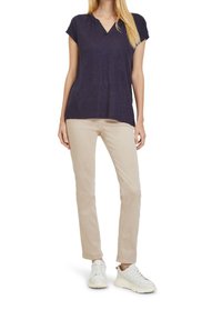 Námořnické tričko s krátkým rukávem a výstřihem do V, se skladem; spárované s světle béžovými kalhotami a bílými teniskami, které ukazují uvolněný střih.