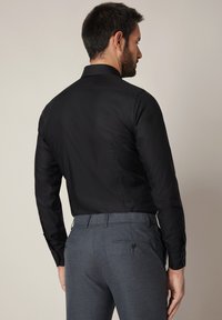 Czarna koszula z długim rękawem o standardowym kołnierzyku, dopasowanym kroju i mankietach na guziki, w połączeniu z szarymi spodniami z tylnymi kieszeniami.