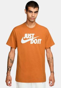 T-shirt in cotone arancione con grafiche "JUST DO IT" bianche, maniche corte, scollatura a giro e vestibilità morbida. Retro semplice e senza motivi visibili.