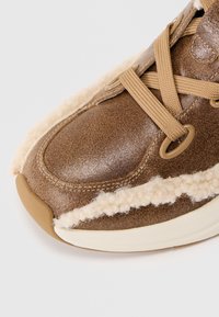 Tenis cu piele maro, având un accent de lână bej pe lateral, prezentând șireturi bej împletite și un design cu vârf rotunjit.