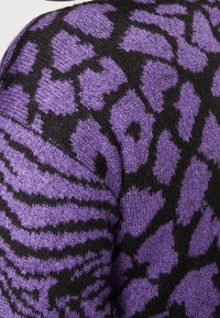 Lila gestrickter Pullover mit einem schwarzen Tiermotiv, das aus verschiedenen Texturen besteht. Das Design umfasst unregelmäßige Formen und Streifen.