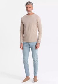 Vaaleanbeige pitkähihainen paita pyöreällä kaula-aukolla, yhdistettynä vaaleansinisiin slim fit -farkkuihin ja vaaleanbeigeihin liukujalkineisiin, neutraalia taustaa vasten.