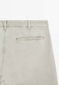 Hellgraue Baumwollhosen mit glatter Textur. Verfügt über eine einfache Gesäßtasche und Gürtelschlaufen. Keine sichtbaren Muster oder Akzente.