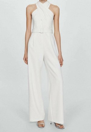Kvinde iført hvid halterneck-jumpsuit med bælte i taljen og bukser med vide ben, parret med sølvfarvede åbne hæle.