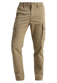 Beige cargo-housut, jotka on valmistettu puuvillasta. Ominaisuuksiin kuuluvat sivutaskut, normaali istuvuus, vetoketjuluukku ja nappikiinnitys. Sileä pinta.