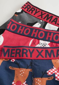 Trei perechi de lenjerie festivă: gri cu omuleți de zăpadă, roșie cu textul "HO HO HO" și albastră cu reni. Fiecare are un brâu ribat.