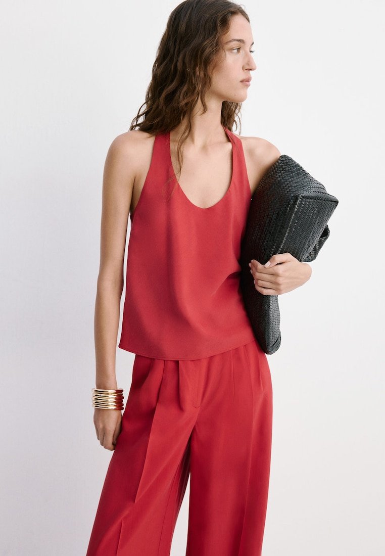 Femme portant un haut rouge sans manches et un pantalon large assorti, tenant une grande pochette noire tissée.
