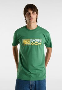 Camiseta de algodón verde con mangas cortas que presenta un diseño gráfico en amarillo y blanco de "VANS OFF THE WALL" en la parte frontal.