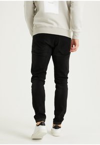 Pantalones vaqueros negros de mezclilla con un corte ajustado, que presentan bolsillos traseros y puños estrechos, combinados con zapatillas blancas con detalles negros y un sudadera gris claro.