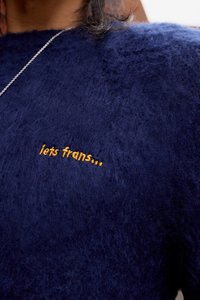 Mørkeblå fuzzy sweater med en blød tekstur og en broderet tekst i gul, der siger "let's trans..." nær halsudskæringen.
