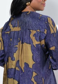 Blusa floral en satén azul y dorado, con un plisado en la parte posterior, escote redondo y mangas largas. Acentuada con patrones abstractos y atrevidos.