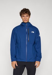 Μπλε αδιάβροχο μπουφάν με φερμουάρ μπροστά, ρυθμιζόμενη κουκούλα και ελαστικές μανσέτες. Διαθέτει λογότυπο και τσέπη με φερμουάρ στο στήθος. Ελαφρύ υλικό.