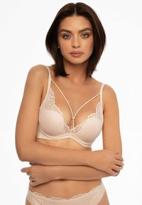 Różowy koronkowy biustonosz o głębokim kształcie litery V, z falbaniastymi brzegami i regulowanymi ramiączkami. Posiada ozdobny detal na środku między miseczkami.