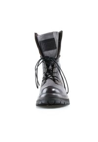 Botte en cuir noir avec lacets défaits, fermeture éclair ouverte sur les côtés et languette pliée montrant un patch avec texte en relief.