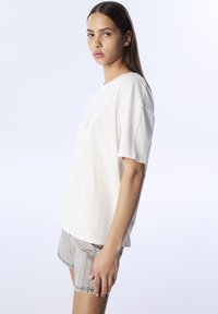 Camiseta blanca de manga corta hecha de algodón, con un detalle impreso en el pecho y combinada con pantalones cortos de color gris claro con patrón.