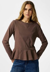 Brun langermet topp med rund hals og peplumkant, laget av mykt stoff, kombinert med blå denimjeans. Enkel og tettsittende design.