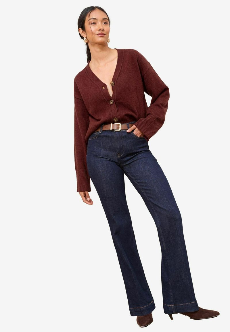 Cardigan oversized burgundiu cu nasturi, asociat cu blugi dark blue evazați. Ținuta include o curea maro și pantofi cu toc maro.